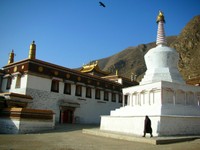 A lone pilgrim circumambulates one of Labrang's white stupas while a lone bird flies overhead.