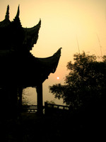 The sun setting behind a pagoda and some bamboo above the Giant Buddha's head.